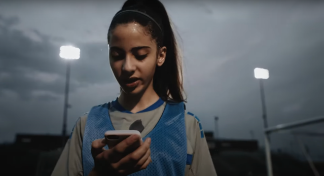 Girl wearing blue soccer pinny after practice and looking down at her phone